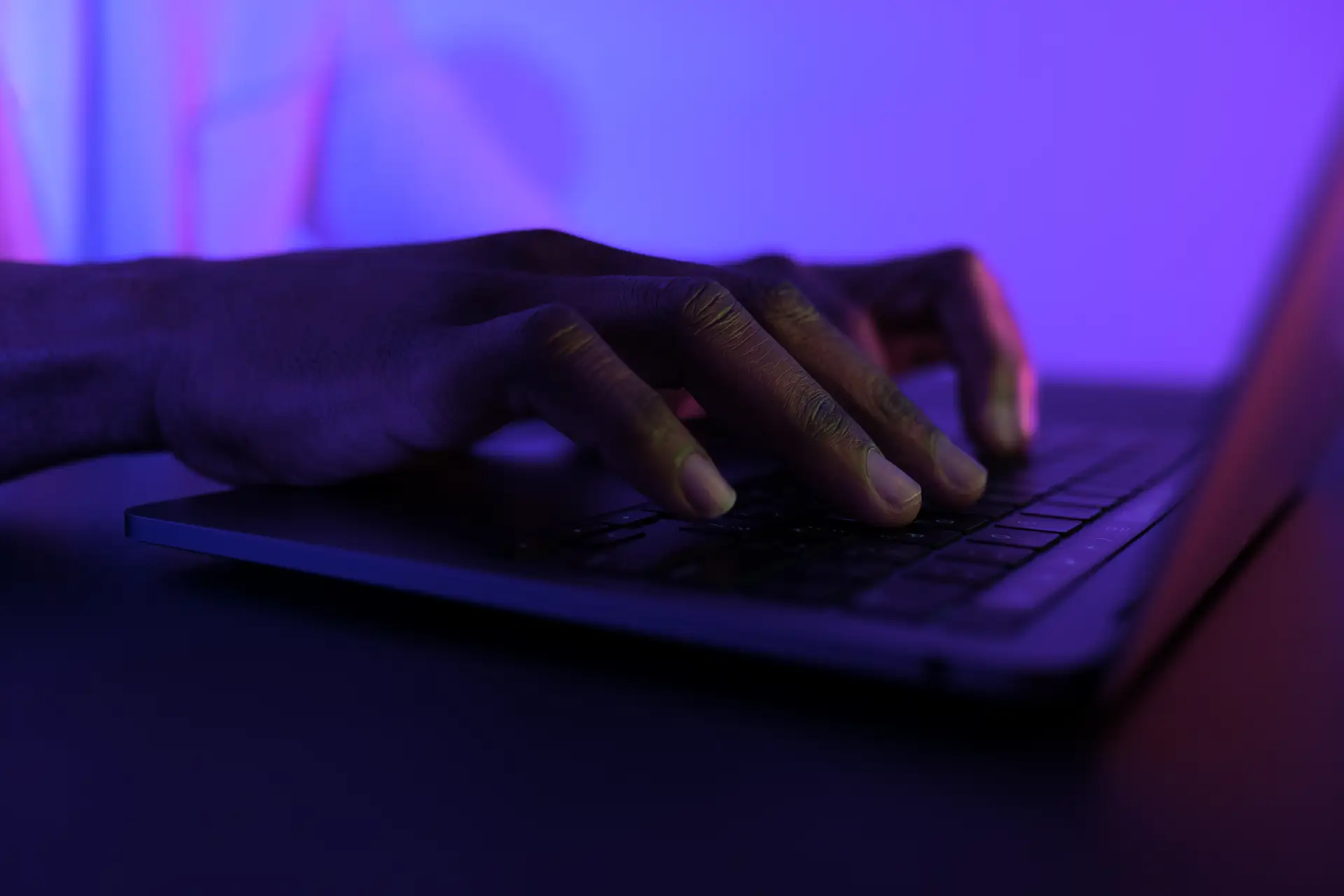 hand typing on laptop with purple filter